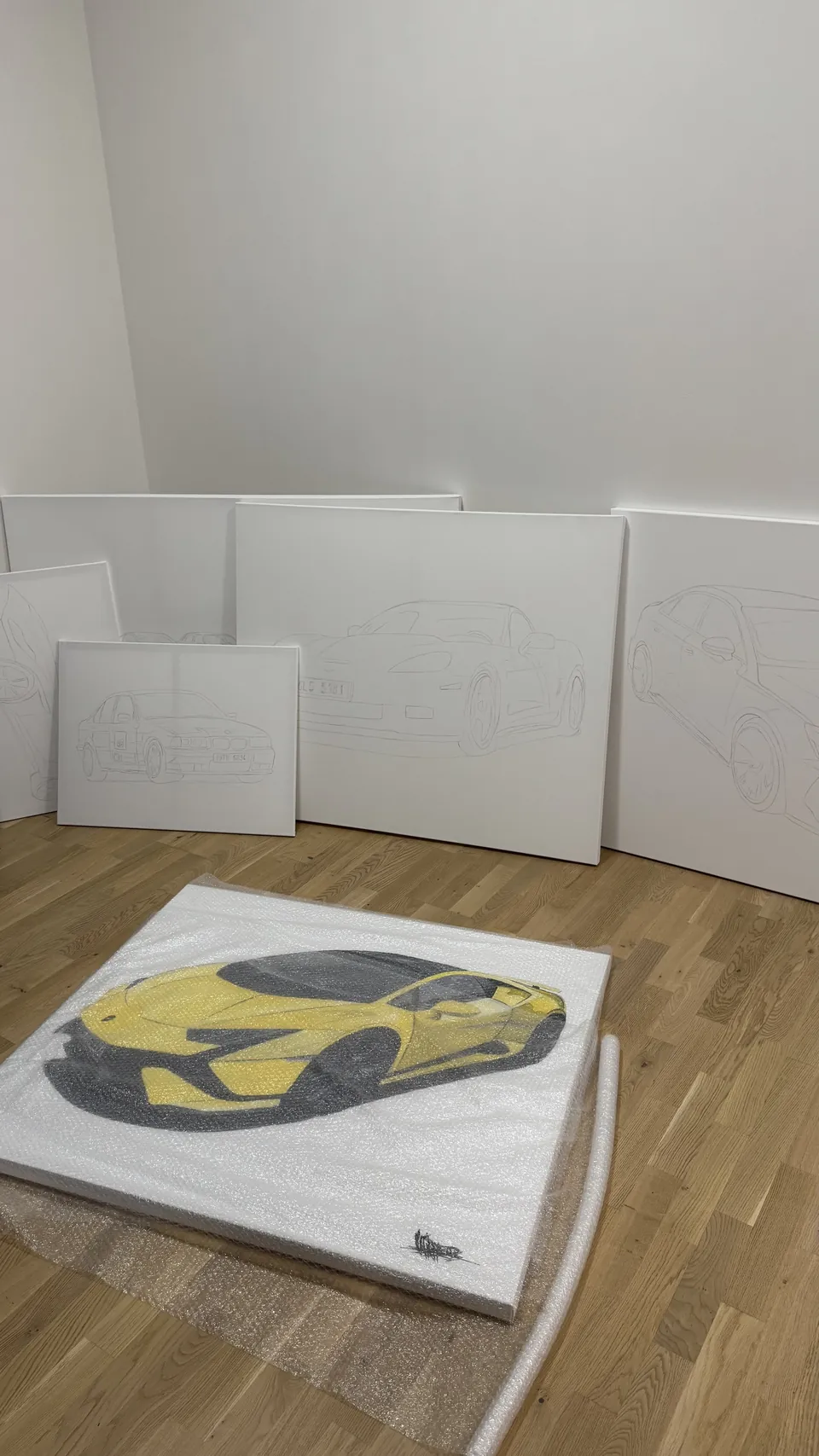 Hotový obraz žlutého Lamborghini na podlaze ateliéru, za ním plátna s předkreslenými vozy
